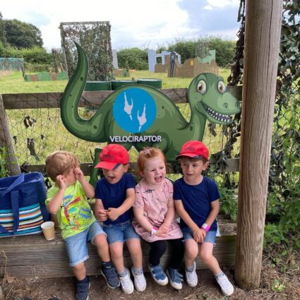 children having fun at dinosaur event sitting in front of a velociraptor dinosaur cutout
